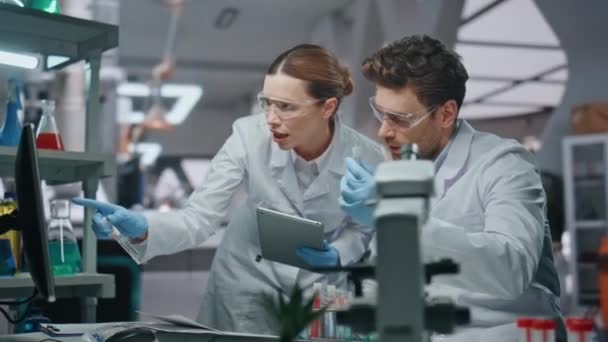 在现代实验室中 女性生物化学家与男性同事就医学研究进行了密切的讨论 两个忙碌的科学家戴着手套看计算机数据 两个实验室的医学专家一起工作 — 图库视频影像
