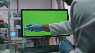 Eldivenler test tüpünü alıp laboratuardaki yeşil ekran bilgisayara araştırma verilerini giriyor. Modern laboratuvarda numunelerle çalışan tanınmayan bir doktor. Klinikteki Chroma Key PC 'de yazan kimyager
