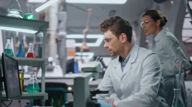 Modern laboratuvarda çalışan iki bilim adamı yakın çekim yapıyor. Bilgisayar monitörüne bakan gülümseyen laboratuar arkadaşları klinikte araştırma yapıyorlar. Dost canlısı kadın kimyager ve tablet danışmanı erkek stajyer..