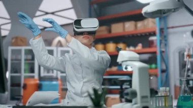 VR gözlüklü doktor artırılmış gerçeklik simülasyonunu kontrol ediyor modern laboratuvarda araştırma yapıyor. Kadın bilim adamı ellerle görünmez arayüzü hareket ettiriyor. Gözlüklü bir araştırmacı siber uzayda çalışıyor