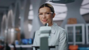 Modern yenilik laboratuarında kamera arayan profesyonel biyokimya araştırmacısı. Tıp laboratuarında başarılı bir bilim adamının portresi. Gelişmiş klinikte oturan genç bayan bir uzman..