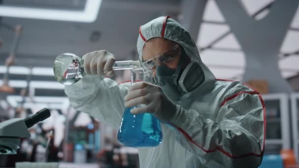 保護スーツを身に着けている化学液体が付いている生化学薬品の詰物の実験室のフラスコ 安全手袋の危険物質を調べる真剣な科学者 ワクチンに取り組むプロの化学者 — ストック動画
