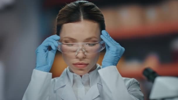 医療クリニックで働くための保護眼鏡を身に着けている実験室の化学者 顕微鏡を検査する美しい女性科学者 研究室で新しいワクチンを研究する真剣な医師 — ストック動画