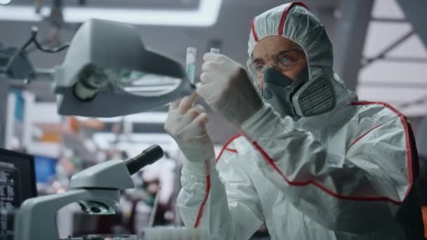 Chemistry expert researching virus in protective uniform at innovation laboratory close up. Skilled chemist looking microscope holding test tubes. Man scientist in hazmat mask making experiment.