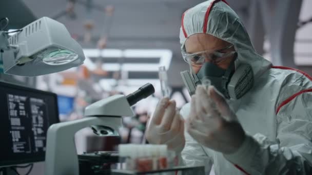 安全スーツの実験室で働くラボ化学者が近づいています テスト管の化学物質を調べる真剣な男性科学者 クリニックで顕微鏡を見るプロのバイオテクノロジスト — ストック動画