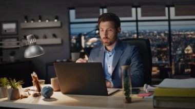 Akşam ofiste dizüstü bilgisayarda çalışan yorgun bir adam. Panoramik pencerelerde bilgisayar okuyan odaklanmış bir işadamı. Çok çalışan girişimci görünümlü ekran çözme görevleri yaratıcı gece alanı