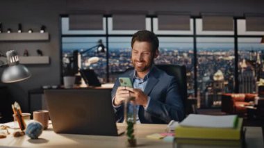 Gülen patron, gece ofisinde akıllı telefon mesajı okuyor. Mutlu iş adamı masadan iyi haberler alıyor. Neşeli bir adam panoramik pencerelerde gülümseyen cep telefonuna bakıyor. Liderlik kavramı 