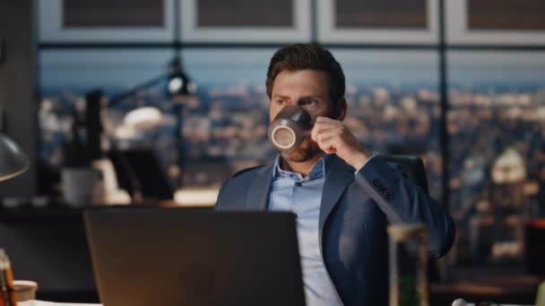 ナイトオフィスの閉鎖でお茶を飲む広範なビジネスマン コンピューターモニターの前に座って休憩を取る集中ディレクター 暗いキャビネットでタスクを解決する準備を飲料を楽しむ忙しい深刻なボス — ストック動画