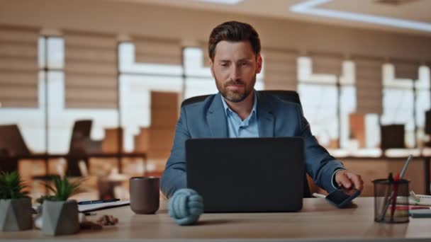 积极的老板把在现代机构工作的手机放下了 微笑英俊的商人看着笔记本电脑屏幕 在平静的气氛中准备演示 留胡子的经理坐在电脑桌前 — 图库视频影像