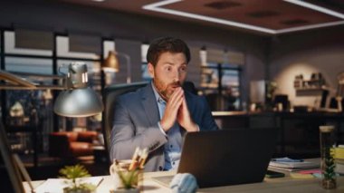 İşadamı karanlık modern ofiste bilgisayarla çalışırken başarılı olduğunu hissediyor. Mutlu gülümseyen yönetmen finans şirketinin sonuçlarını tatmin etti. Esmer girişimci bilgisayar ekranında harika haberler okuyor. 