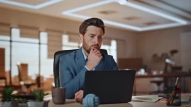 Panoramik ofiste bilgisayarla çalışan odaklanmış bir iş adamı. Esmer sakallı patron, modern iş binasındaki bilgisayarla iş anlarını çözüyor. CEO tek başına yatırım stratejisi düşünüyor.