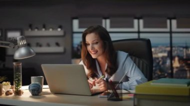Patron gece görüş ofisinde bilgisayarla görüntülü konuşma yapıyor. Gülümseyen bayan, müşterisiyle sanal konferansta olumlu bir yüz ifadesiyle konuşuyor. Güleç iş kadını kabineye bilgisayar görüntülerini iletiyor. 