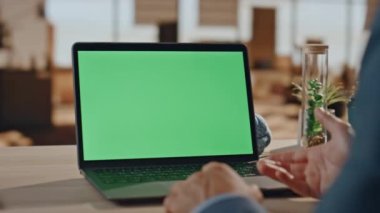 Yakından bir iş adamı ofisteki yeşil ekran bilgisayarına video çağrısı yapıyor. Tanımlanamayan patron dijital cihaz yakınlaştırması kullanıyor. Çalışma masasındaki krom anahtar dizüstü bilgisayara el hareketi yapan bir erkek. 