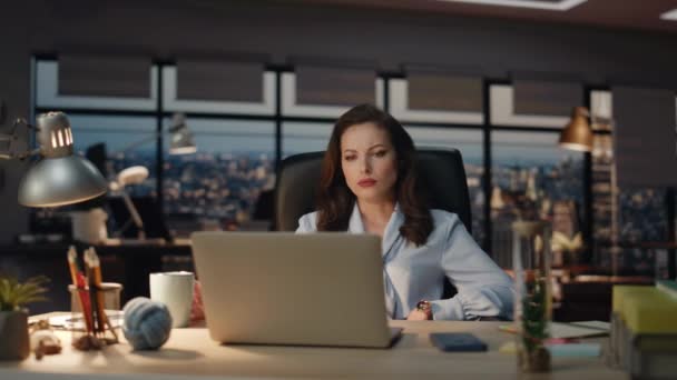 ダークオフィスの閉鎖に遅く滞在する女性のワークホリック 画面に焦点を当てようとしているノートパソコンの電子メールを分析する疲れたマネージャー ブルネット ビジネスウーマン パノラマウィンドウキャビネットで一人で働く — ストック動画