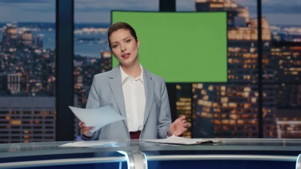 放送スタジオで報道する女性ニュースプレゼンター 緑色のスクリーンディスプレイのニュースルームでテキストだけで紙をチェックするポジティブな女性 モックアップクロマキー画像背景で話すエキスパートアンカー — ストック動画