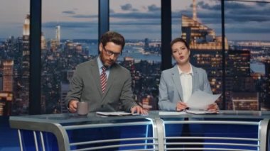 Ekip muhabirleri canlı haber stüdyosundan akşam haberlerini kapatıyorlar. TV kanalında birkaç sunucu haber bültenine başlıyor. Kendine güvenen sunucular televizyon izleyicileriyle etkileşimde.