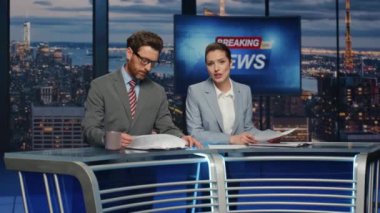 Kendine güvenen sunucular akşam haberleri sunuyor modern stüdyo kapanışı. Profesyonel televizyon sunucuları haber odasında birlikte yayın yapıyorlar. Seçkin çift, günlük haber bültenini aydınlatıyor.