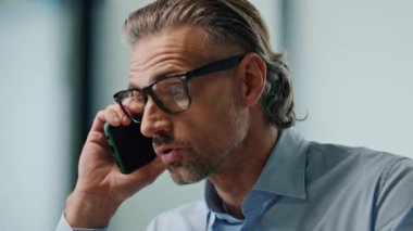 Sinirli yönetmen akıllı telefon görüşmesini kapalı mekândaki portrede tartışıyor. Sinir bozucu yönetici yakın çekimde cep telefonuyla konuşuyor. Stresli iş adamı iş yerinde ses tonuyla konuşuyor. Çalışma sorunları kavramı