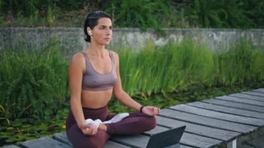 Park bankında sakinleştirici Yogini meditasyon tableti. Nilüfer çiçekli orta yaşlı, dingin bir kadın poz veriyor ve internet dersini izliyor. Gülümseyen sporcu kadın yoga yapıyor müzik dinliyor. Kulaklıklı düşünceli bayan.