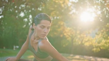 Güneş ışınları parkında esnek bir kadın vücudu büküyor. Zayıf orta yaşlı sporcu kadın yeşil doğada tek başına omuz geriyor. Bronzlaşmış kaslı kadın ısınıyor, dışarıda idman yapıyor.