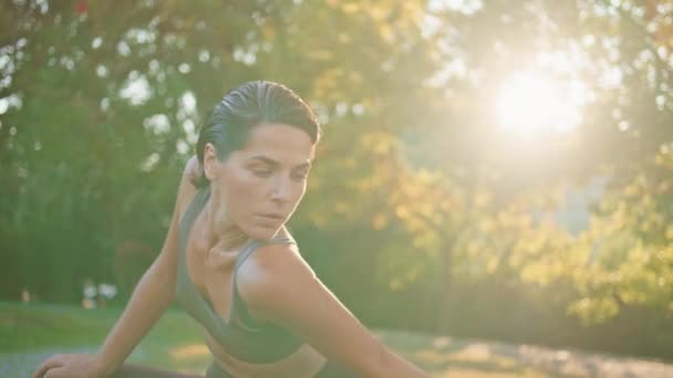 サンビーム公園のクローズアップで体を曲げる柔軟な女性 緑の自然で一人で運動する肩を伸ばすスリムな中年スポーツウーマン トレーニングアウトドアにフィットすることを温める予定の筋肉女性 — ストック動画
