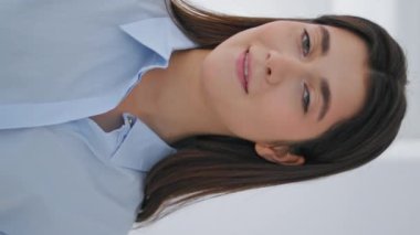 Gülümseyen iş kadını kameraya yakından bakıyor. Modern beyaz iş merkezi dikey videosunda mutlu menajer saçına dokunuyor. Sanat galerisinde çalışan neşeli kadın sanatçı. Kendine güvenen girişimci..