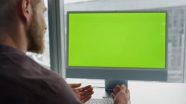 Gesturing freelancer virtual call at chromakey monitor office. Friendly specialist speaking mockup computer at panoramic windows room closeup. Man using green screen pc device video technologies alone