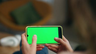 Oyuncu evde kromakey oynayan cep telefonu kullanıyor. Kimliği belirsiz bir kadın salonda tek başına akıllı telefon ekranına dokunuyor. Modern kız elleri video oyunu oynarken yeşil ekran cep telefonunu tıklatıyor