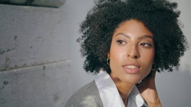 Portrait of sensual attractive model with curly hairstyle in front stone wall. Gorgeous african american woman face illuminated summer sunlight. Young beautiful girl posing outdoors sunny day close up