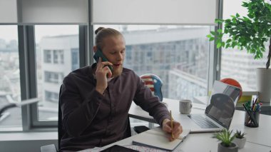 Neşeli serbest çalışan ev ofisinden cep telefonunu arıyor. Gülümseyen tasarımcı hipster apartmanında telefonla ilgili notlar yazıyor. Laptop masasında oturan yakışıklı adam yalnız çalışıyor. Teknoloji konsepti 