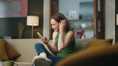 Evde cep telefonuyla konuşan gülen bir kadın. Cep telefonuyla gülümseyen kadın evde tek başına şakalar izliyor. Rahatlamış kaygısız kız akıllı telefon ekranında komik mesajlar okuyor.