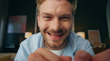 Gülen iş adamı web kamerasından oda görüntüsüne sesleniyor. Pozitif adam başını sallayarak başını sallıyor. Kapalı mekanda konuşulanları dinliyor. Duygusal gülümseyen adam ev içi portrede görüntülü sohbetten hoşlanıyor.