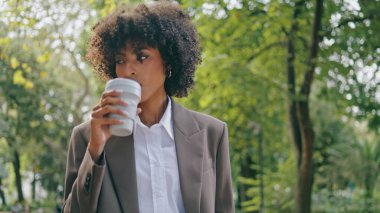 Molada şehir parkında gezen rahat stil sahibi bir kadın kahve servisinin keyfini çıkarıyor. Kendine güvenen Afro-Amerikan iş kadını kağıt bardakta içecek içiyor. Akıllı telefonlu çekici bir kız..