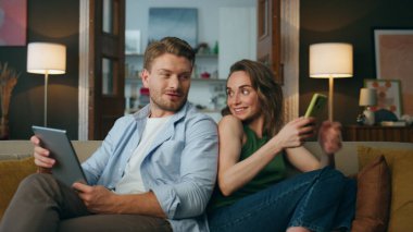 Konuşan çiftler kanepeyi yakınlaştırıyor. Kanepeye yakın otururken telefonu kullanan gülümseyen kadın. Evde tablet bilgisayar ve kitap okuyan olumlu bir adam var. İnternet bağımlısı aile hafta sonu konsepti