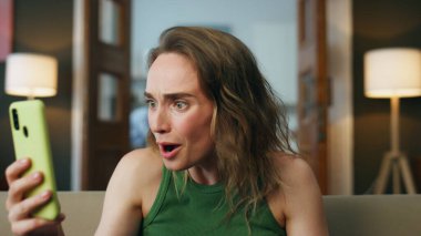 Evde akıllı telefondan şüphelenen şaşırmış bir bayan var. Cep telefonu mesajını okuyup kanepe odasında 