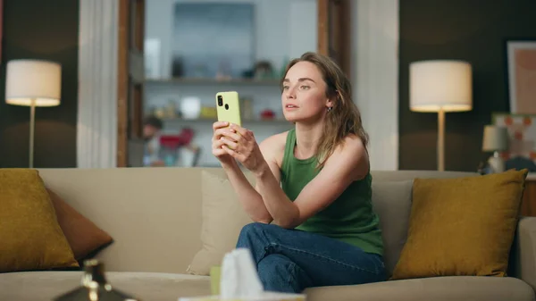 Serious businesswoman talking smartphone at home office. Focused freelancer lady having video chat at domestic atmosphere. Involved woman using phone sitting sofa. Girl looking at cellphone camera
