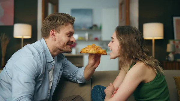 Romantic pair eating croissant at home zoom on. Loving man woman face bitting french bun from different sides super closeup. Cute lovers enjoying tasty food at breakfast. Happy family morning together