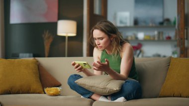 Telefon koltuğunu kullanan gergin bir bayan. Stresli kız, akşam odasında akıllı telefon okuyor. Memnuniyetsiz bir kadın. İç mekandaki bozuk alet. Koltuğa cep telefonu atan duygusal bir kadın. 