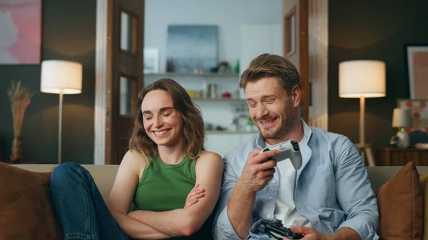 Smiling man giving gamepad to wife at home pov. Laughing woman taking joystick sitting sofa at living room zoom on. Domestic married pair enjoying videogame activity. Two people evening leisure time