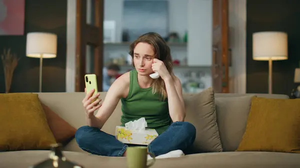Depressed woman phone calling at couch interior. Frustrated lady talking psychotherapist at online session. Sad girl holding napkin suffering of problems at videocall therapy. Mental health concept