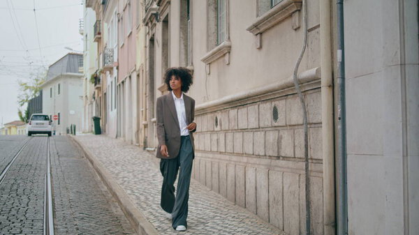 Stylish carefree woman walking trowalk wonderful city street exploring district alone. Уверенная африканская американка спокойно прогуливается по городу в летние выходные. Кудрявая леди наслаждается отдыхом в городе.