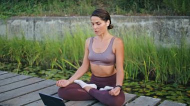 Green Park 'ta meditasyon yapan kadın yoga egzersizleri yapıyor. Nilüfer çiçekli huzurlu bayan yazın uzaktan eğitim veriyor. Tablet bilgisayarında asana dersi veren kulaklıklı spor eğitmeni.