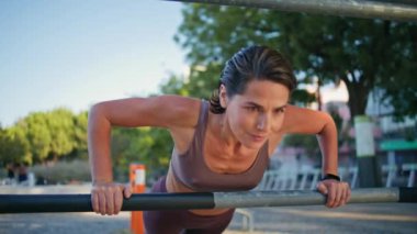 Yaz sokak portresi için kadın pazılarını çalıştırmaya odaklanmış. Açık hava spor salonunda egzersiz yapan aktif bir kadın. Yakın plan. Yatay çubuk kullanarak tahta görünümlü kamerada fitness eğitmeni