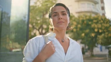 Şehir merkezindeki fotoğrafta mutlu iş kadını görüntüsü var. Summer City 'nin yakın çekimlerinde poz veren gururlu bir kadın. Başarılı orta yaşlı yönetici kasabada gülümseyen bir çanta tutuyor. Yoğun yaşam tarzı