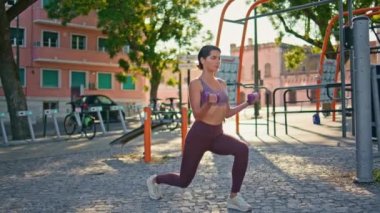 Kas yığını sporcu kadın sokak antrenmanında dambılları kaldırıyor. Odaklanmış olgun bir kadın tek başına açık hava spor salonunda ağırlık kaldırma eğitimi alarak çömelme hareketleri yapıyor. Sağlıklı yaşam tarzı kavramı 