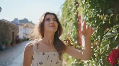 Gülleri koklayan kaygısız bir kadın çiçeklere dokunuyor. Gülümseyen turist kadın hafta sonu dinlenen doğaya bakıyor. Çekici kız tatilde kırsal küçük sokakların tadını çıkarıyor.