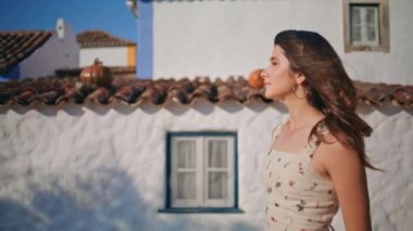 Güneşli köyde gezen hayalperest bir kadın. Gülümseyen kız, haftasonu gezintisinde Akdeniz evlerini düşünmekten zevk alıyor. Resimli romantik bayan kırsal tatilde rahatlayan kameraya bakıyor.