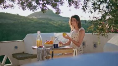 Serene model, dağ manzaralı terasta meyve hazırlıyor. Gülümseyen mutlu kadın üst balkonda yemek yaparken elma kesiyor. Neşeli kız yeşillik köyünde tek başına yemek pişiriyor.