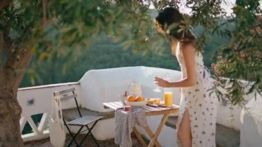 Dağlarda oturan hassas kız doğa manzaralı balkon. Rüzgarlı saçlı kadın yaz terasında kahvaltı hazırlıyor. Esmer, şehvetli bir model elinde suyla bardakla hafta sonunun tadını çıkarıyor.