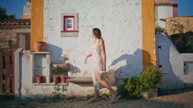 Romantik elbiseli kadın kırsal kesimde tek başına dolaşıyor. Akdeniz köyü düşüncesiyle eski evin camına dokunan turist kadın. Şehvetli bir model kaldırım kenarında yürüyor ve yeni yerlere hayran.